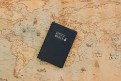 A Holy Bible rests on an antique style world map with vintage hues.